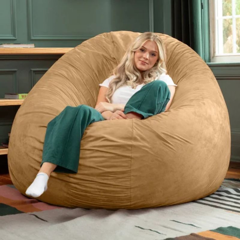 Young woman relaxing in the tan Jaxx Cocoon bean bag chair shaped into an upright cupped seat, a sensory chair for teens and adults