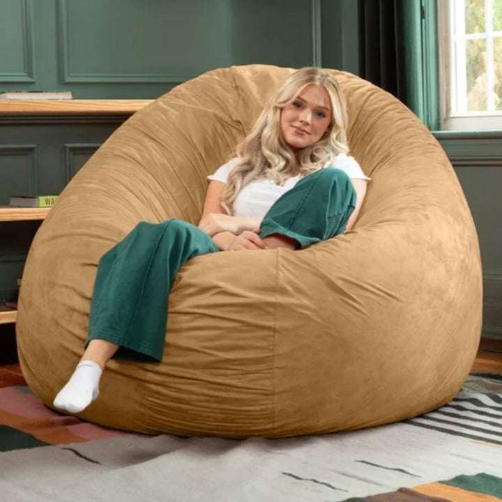 Young woman relaxing in the tan Jaxx Cocoon bean bag chair shaped into an upright cupped seat, a sensory chair for teens and adults