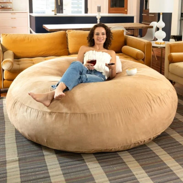 Woman reclining flat on the tan Jaxx Cocoon bean bag chair used as a giant lounger, a sensory seating option for living rooms and calm corners