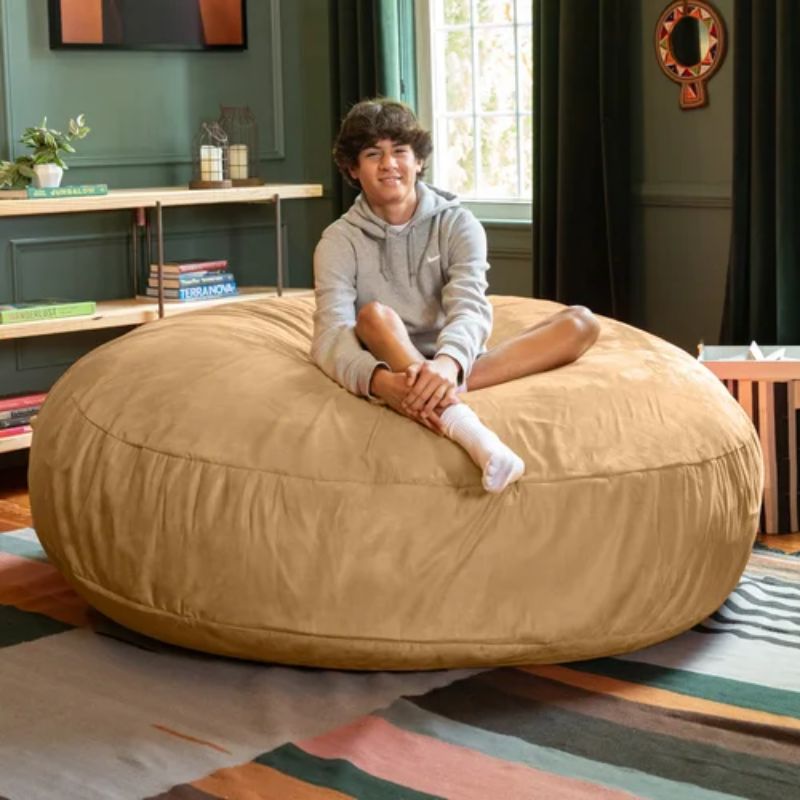 Teen sitting on top of the tan Jaxx Cocoon bean bag chair, a round deep pressure sensory seat for calm corners and family rooms