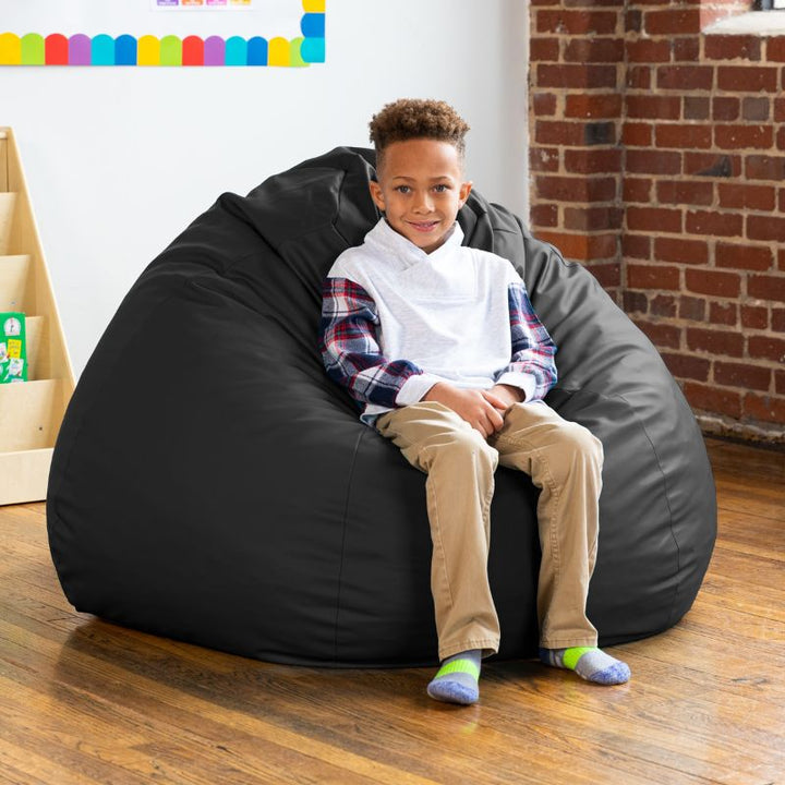 Boy sitting on a black Jaxx Gumdrop kids bean bag chair in a classroom