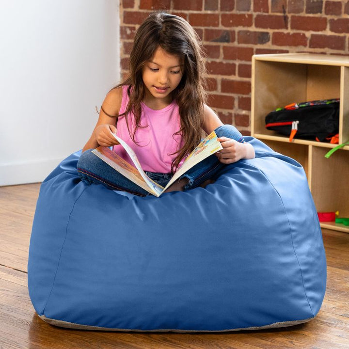 Girl reading a book while seated on a blue Jaxx Gumdrop bean bag chair in a classroom