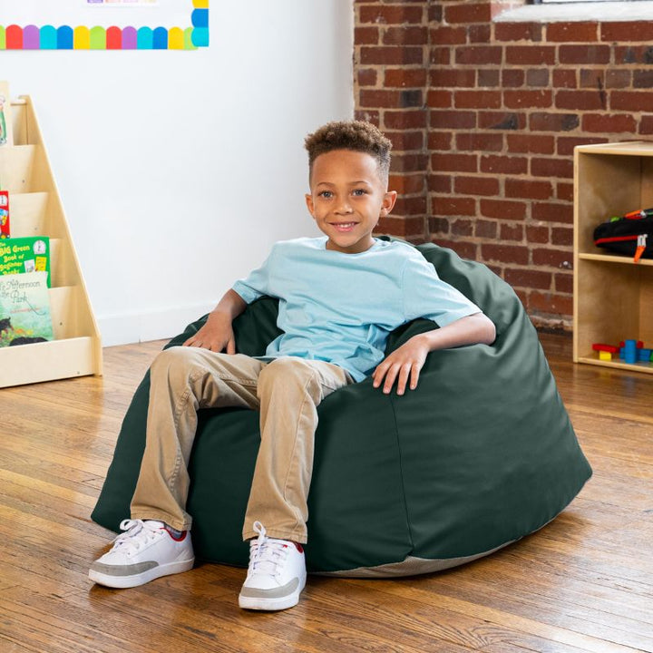 Boy sitting in a dark teal Jaxx Gumdrop bean bag chair, with a classroom reading corner in the background