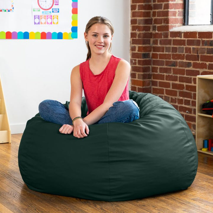 Teen sitting cross-legged on a forest green Jaxx Gumdrop kids bean bag chair in a classroom