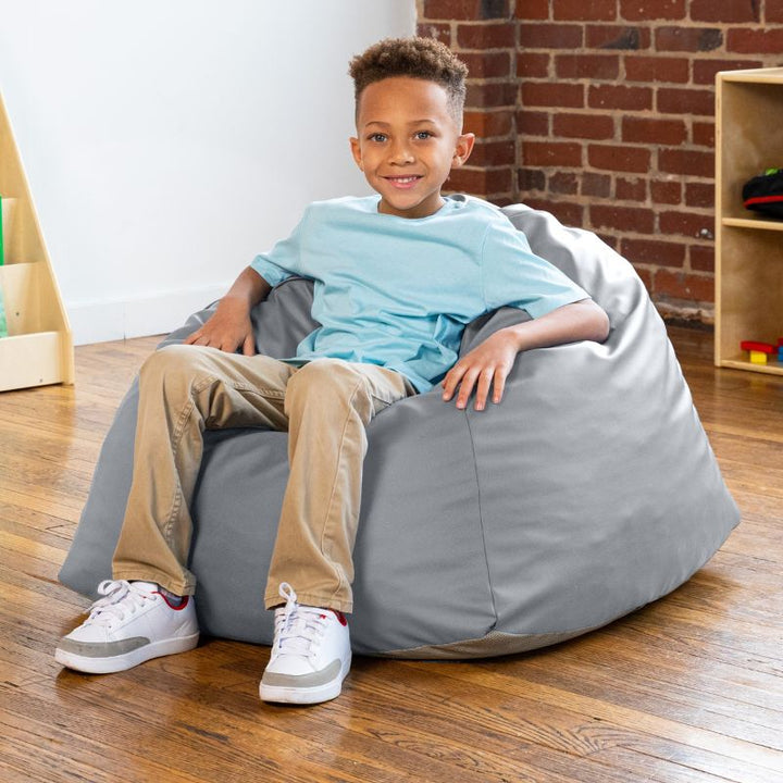 Boy sitting in a grey Jaxx Gumdrop bean bag chair in a classroom setting