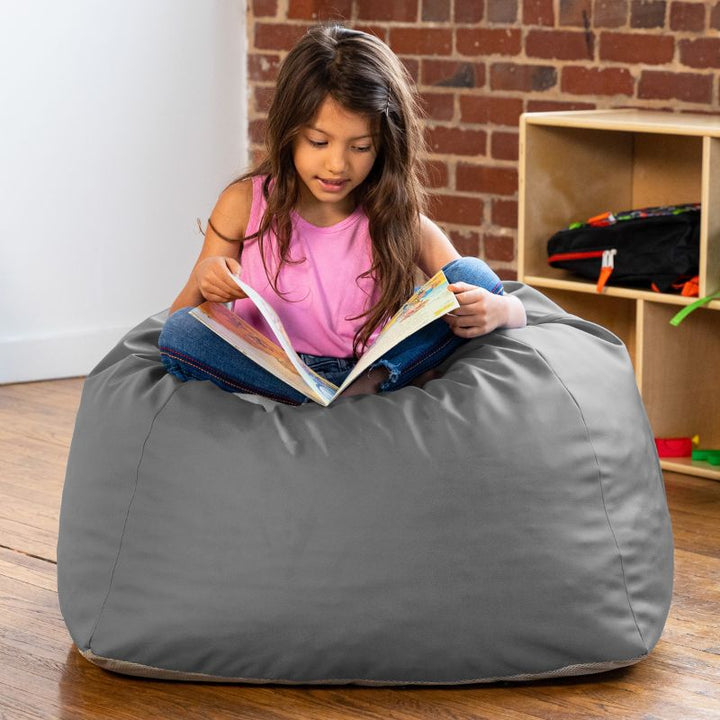 Girl reading a book while seated on a grey Jaxx Gumdrop bean bag chair in a classroom