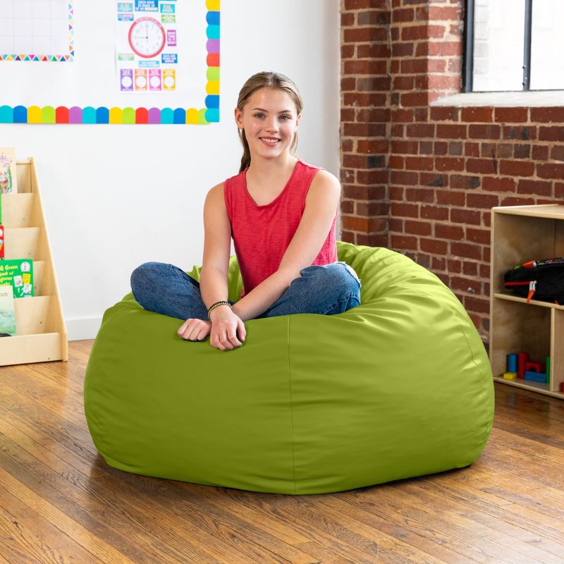 Teen sitting cross-legged on a lime green Jaxx Gumdrop kids bean bag chair in a classroom