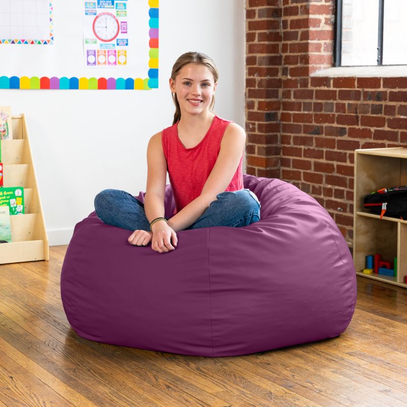Teen sitting cross-legged on a purple Jaxx Gumdrop kids bean bag chair in a classroom