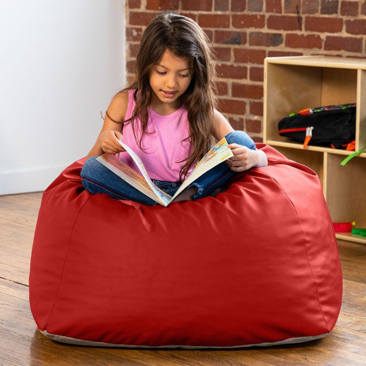 Girl reading a book while seated on a red Jaxx Gumdrop bean bag chair in a classroom
