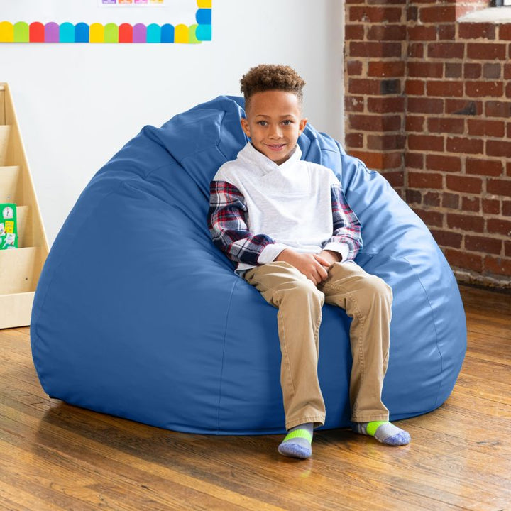 Boy sitting on a royal blue Jaxx Gumdrop kids bean bag chair in a classroom