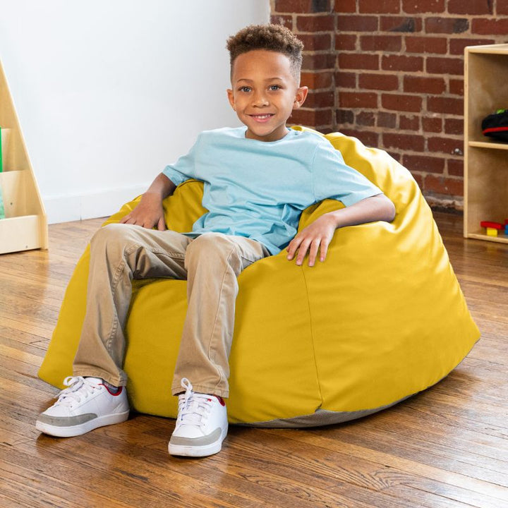 Boy sitting in a yellow Jaxx Gumdrop bean bag chair in a classroom setting
