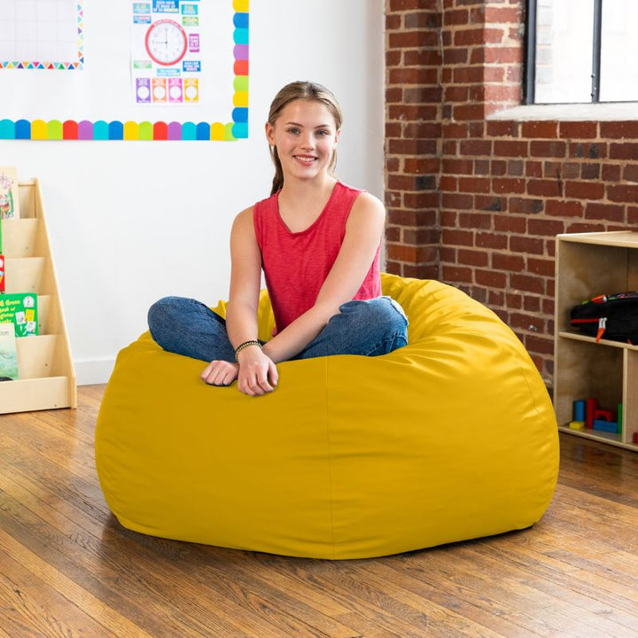 Teen sitting cross-legged on a yellow Jaxx Gumdrop kids bean bag chair in a classroom