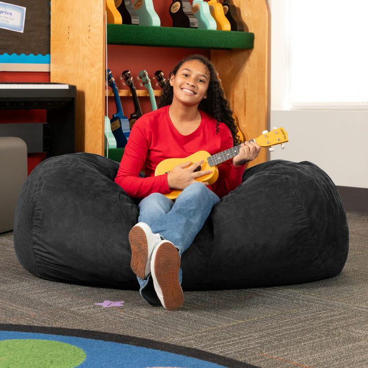 Teen playing ukulele on the Jaxx Lounger 4ft bean bag chair in Black microsuede, a washable sensory seat for classrooms