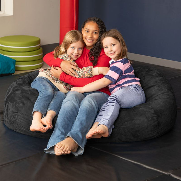 Three children sharing the Jaxx Lounger 4ft bean bag chair in Black microsuede, a washable deep pressure seat