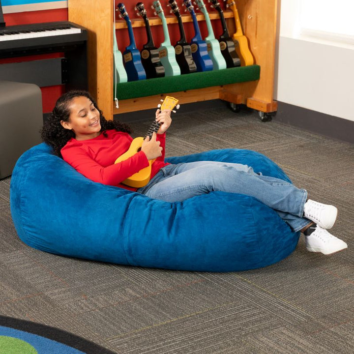 Teen reclining with a ukulele on the Jaxx Lounger 4ft bean bag chair in Blue microsuede, a washable classroom seat