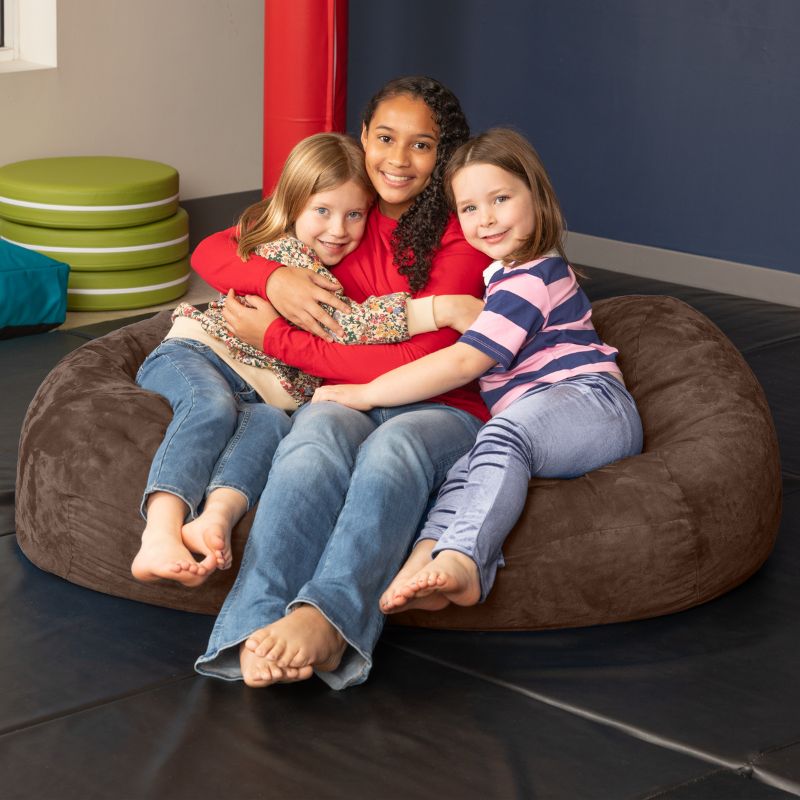 Three children sharing the Jaxx Lounger 4ft bean bag chair in Brown microsuede, a washable sensory room seat