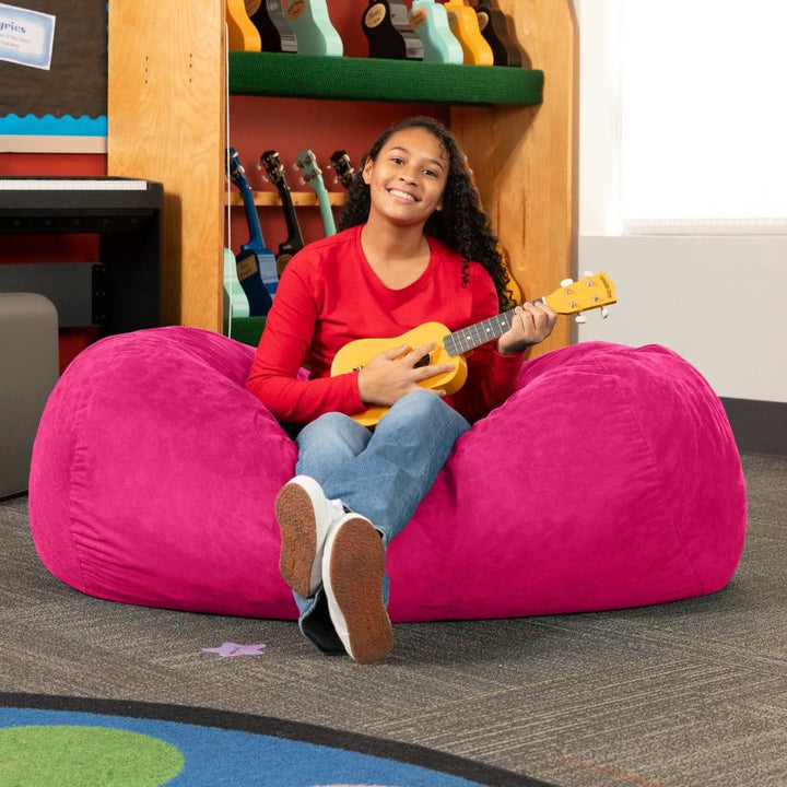 Teen playing ukulele on the Jaxx Lounger 4ft bean bag chair in Pink microsuede, a washable calm corner seat