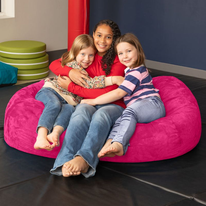 Three children sharing the Jaxx Lounger 4ft bean bag chair in Pink microsuede, a roomy classroom seating option