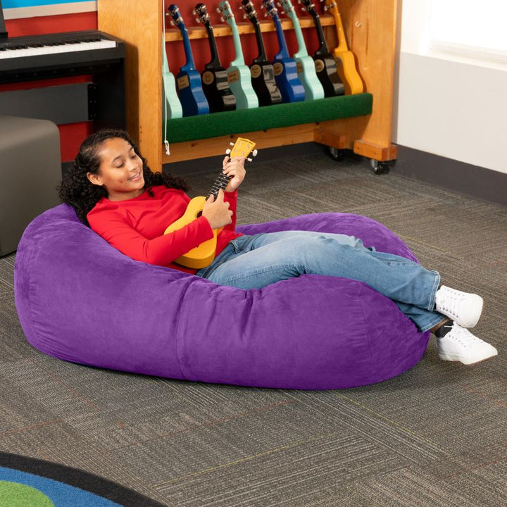 Teen reclining with a ukulele on the Jaxx Lounger 4ft bean bag chair in Purple microsuede, a washable classroom seat