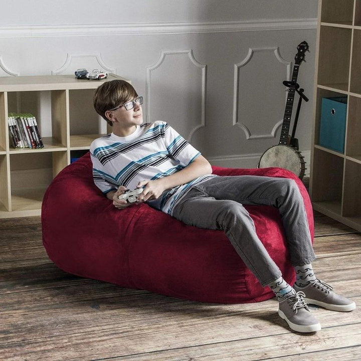 Boy relaxing with a game controller on the Jaxx Lounger 4ft bean bag chair in Red microsuede, a cozy bedroom sensory seat