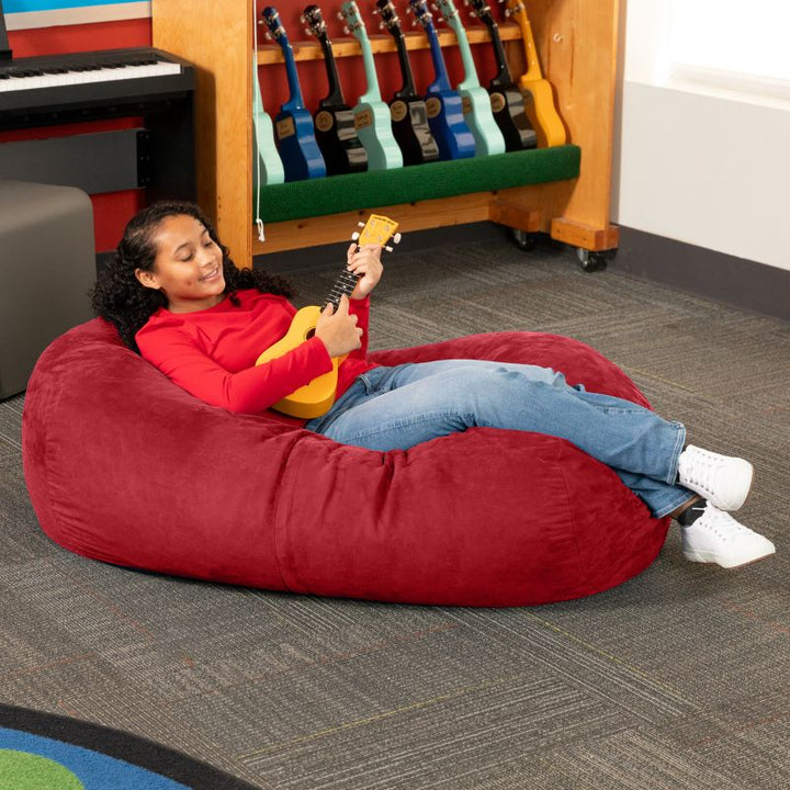 Teen reclining with a ukulele on the Jaxx Lounger 4ft bean bag chair in Red microsuede, a washable calm corner seat