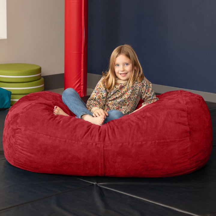 Child sitting on the Jaxx Lounger 4ft bean bag chair in Red microsuede, a washable sensory room seat
