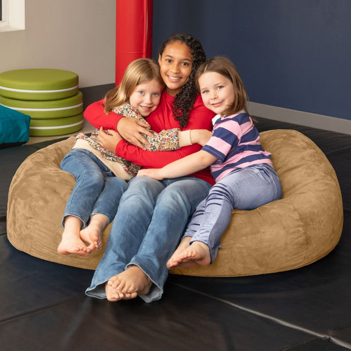 Three children sharing the Jaxx Lounger 4ft bean bag chair in Tan microsuede, a washable seat that fits up to three kids