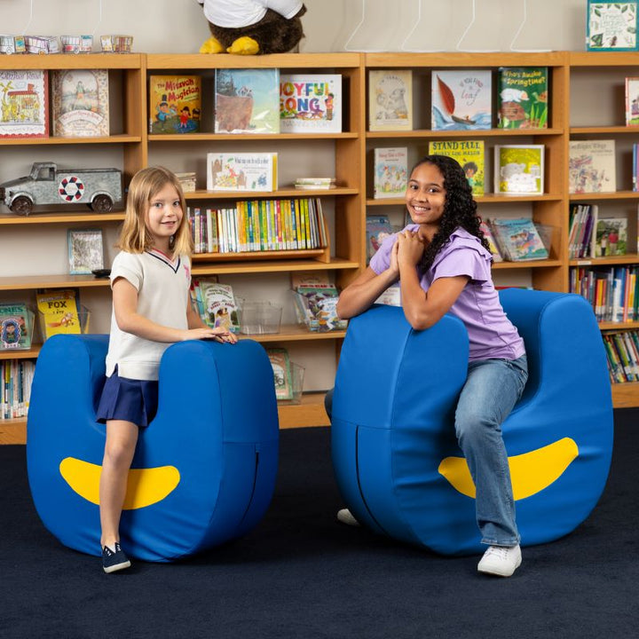 Two children seated on Jaxx Zipline Loveseat units in a school library, shown as flexible soft seating for classrooms