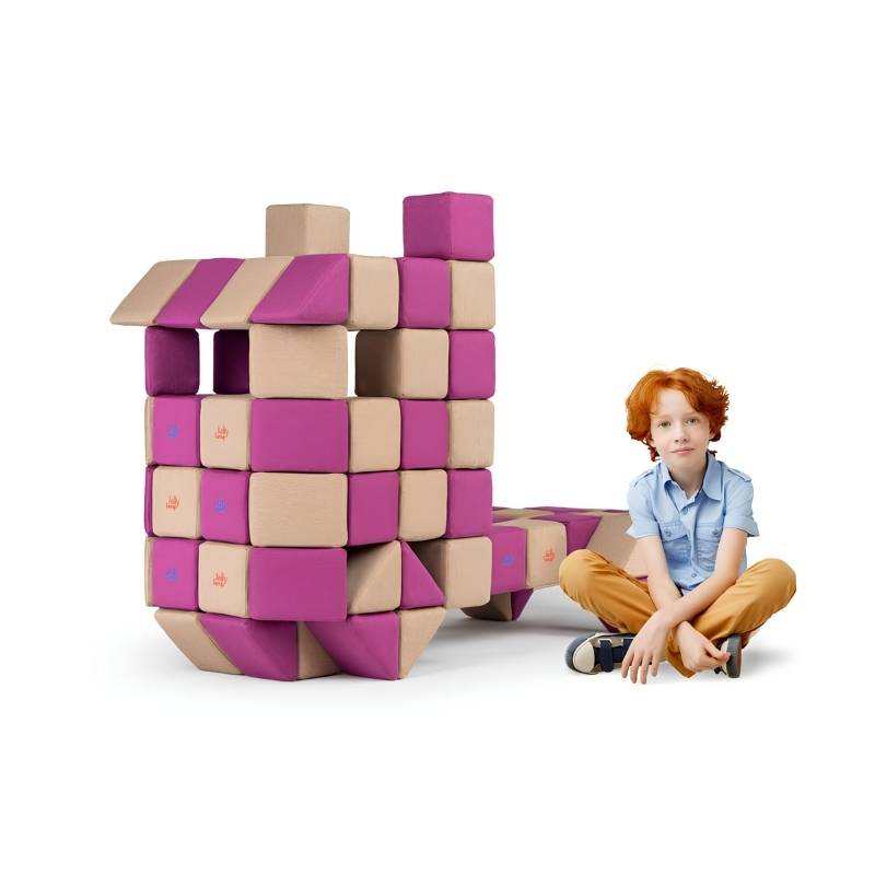 A boy sits beside a tall castle-style structure built from JollyHeap Basic Set magnetic foam blocks, demonstrating the large-scale builds possible with this soft play set.
