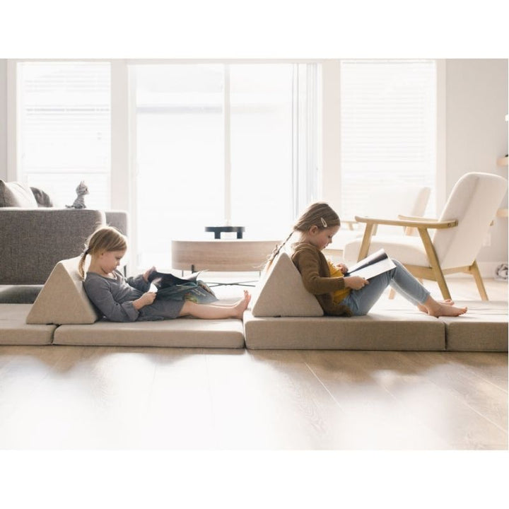 Child resting on the Kiddie Couch in Sand Beige with triangular wedge as back support, showing the sensory play couch in relaxation configuration