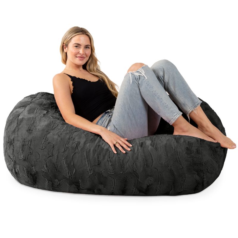A woman sits on the Jaxx Lounger 4ft faux fur bean bag lounger in Black, showing the kids bean bag chair sized for teens and adults too.