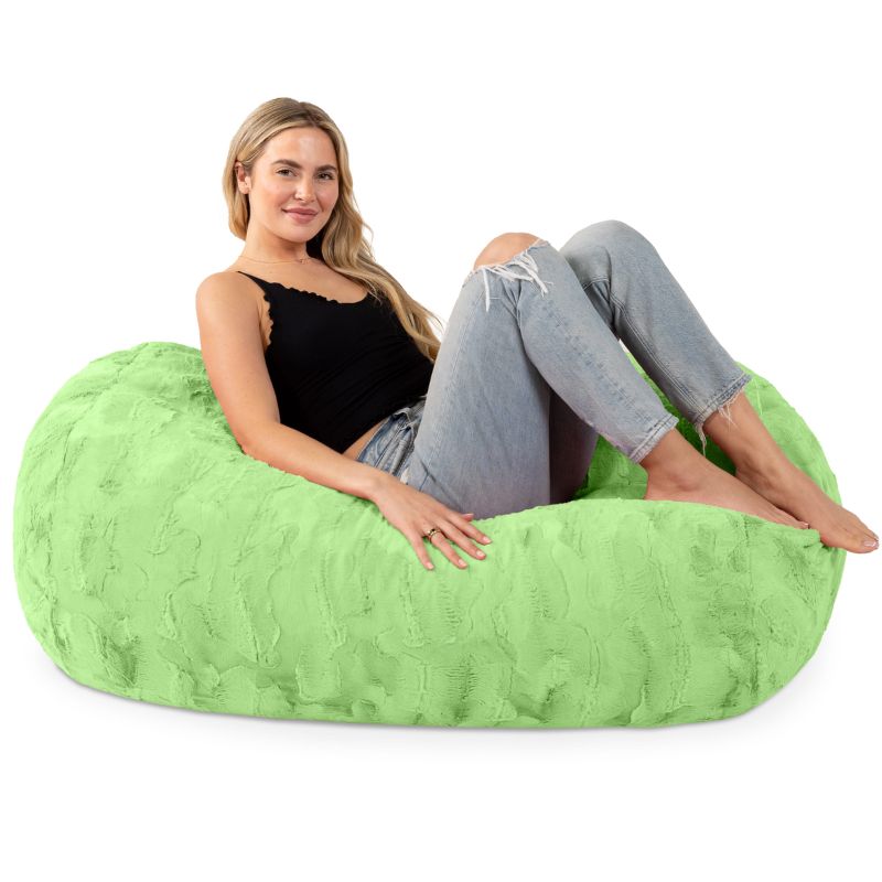 A woman sits on the Jaxx Lounger 4ft faux fur bean bag lounger in Green, showing the kids bean bag chair sized for teens and adults too.