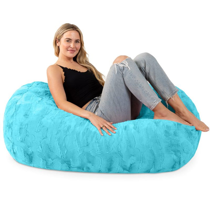 A woman sits on the Jaxx Lounger 4ft faux fur bean bag lounger in Teal, showing the kids bean bag chair sized for teens and adults too.