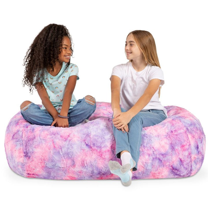 Two girls sit together on the Jaxx Lounger 4ft faux fur bean bag lounger for kids in Unicorn, a pastel tie-dye sensory bean bag chair.