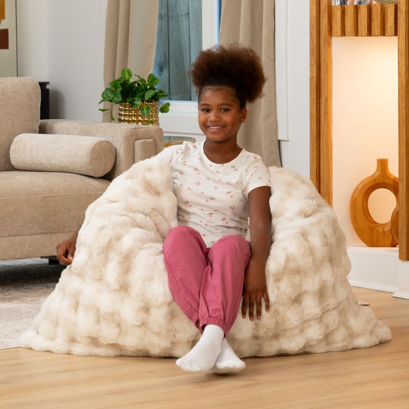 Girl sitting in the CrashPuff by Raven-Symoné faux fur floor lounger propped fully upright in Phantom Cream