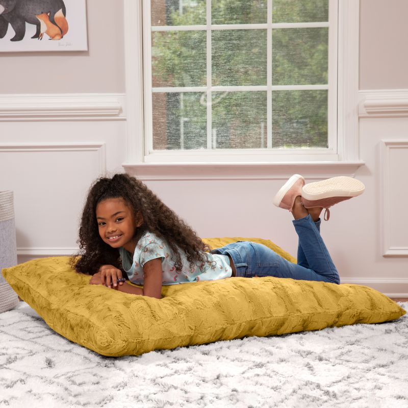 Girl lying flat on the CrashPuff by Raven-Symoné kids faux fur floor lounger in Golden in a bedroom