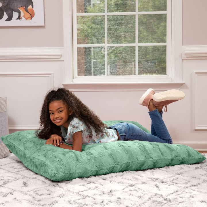 Girl lying flat on the CrashPuff by Raven-Symoné kids faux fur floor lounger in Spearmint in a bedroom