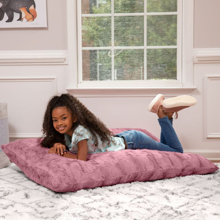 Girl lying flat on the CrashPuff by Raven-Symoné kids faux fur floor lounger in Wild Rose in a bedroom