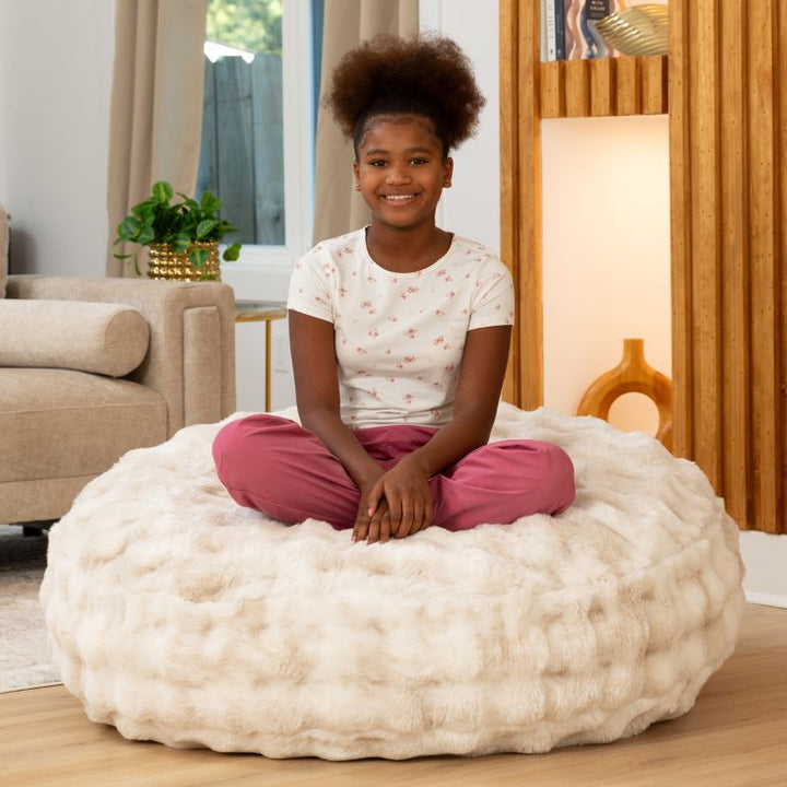 Child sitting cross-legged on the Raven-Symoné Lil' Cuddler kids bean bag lounger in Lush Fur Phantom Cream