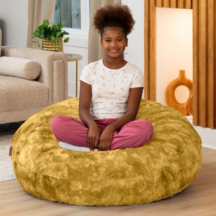Child sitting cross-legged on the Raven-Symoné Lil' Cuddler kids bean bag lounger in Lush Fur Gold