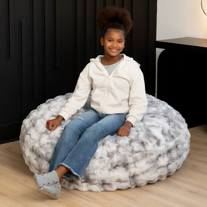 Child sitting on the Raven-Symoné Lil' Cuddler kids bean bag lounger in Lush Fur Phantom Grey, a cozy sensory seat