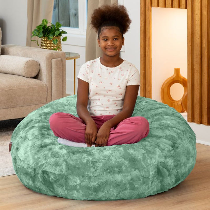 Child sitting cross-legged on the Raven-Symoné Lil' Cuddler kids bean bag lounger in Lush Fur Spearmint Green