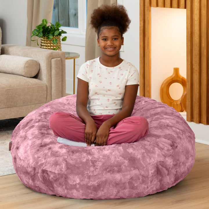 Child sitting cross-legged on the Raven-Symoné Lil' Cuddler kids bean bag lounger in Lush Fur Wild Rose