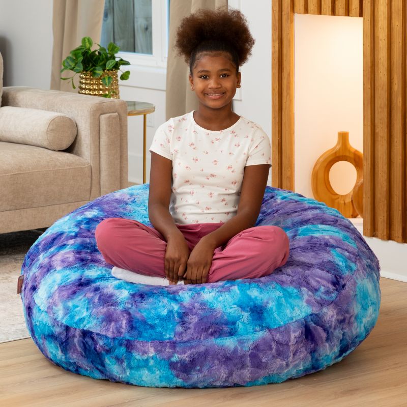 Child sitting cross-legged on the Raven-Symoné Lil' Cuddler kids bean bag lounger in Lush Tie-Dye Fur Mystic Blue & Purple