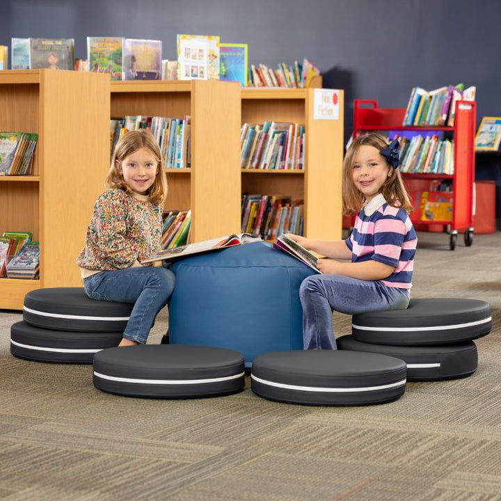 Two children reading in a library while seated on Jaxx Kirkwood black stacking floor cushions around a blue ottoman