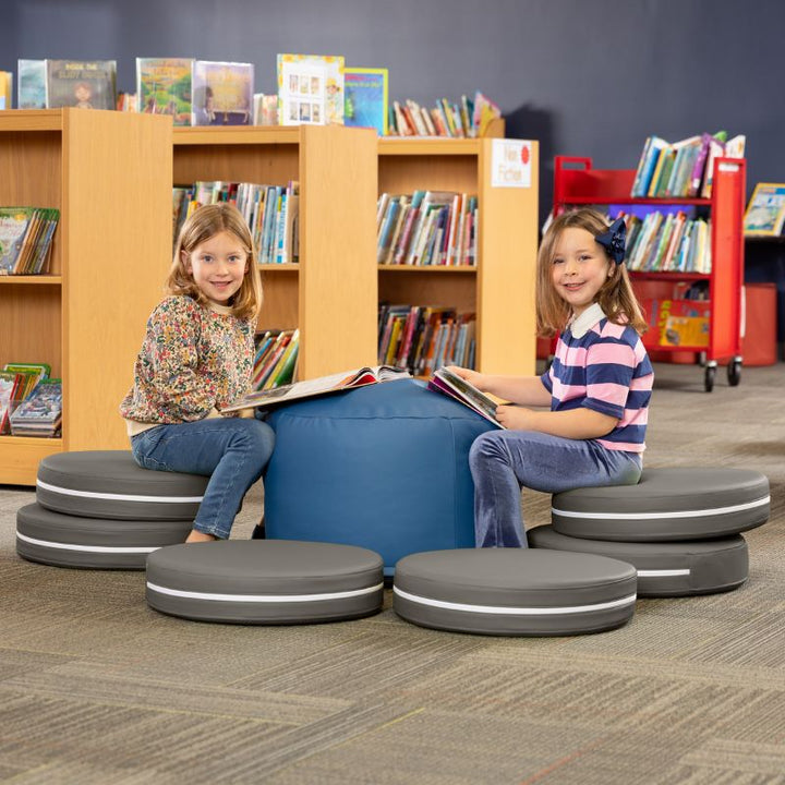 Two children reading in a library while seated on Jaxx Kirkwood charcoal stacking floor cushions around a blue ottoman
