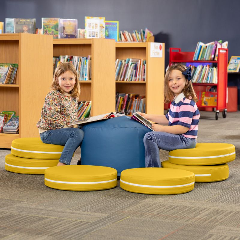 Two children reading in a library while seated on Jaxx Kirkwood yellow stacking floor cushions around a blue ottoman