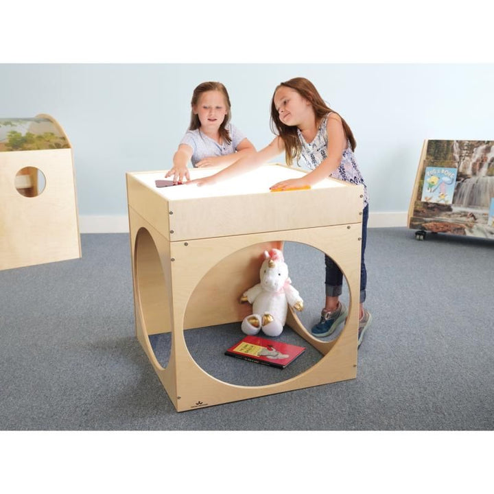 Two girls explore translucent shapes on the glowing top of the Whitney Brothers Superbright LED Creative Cube, a light table reading cube with a reading nook for kids below