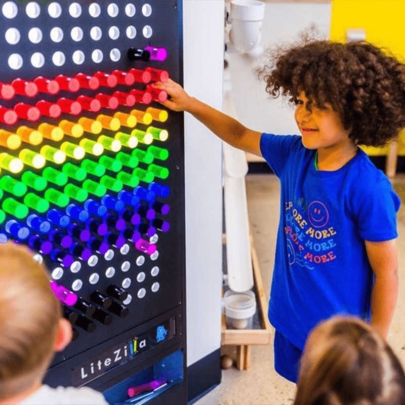 Boy actively playing at the LiteZilla Giant Lite Brite sensory light wall, creating a colourful glowing pattern with LitePins
