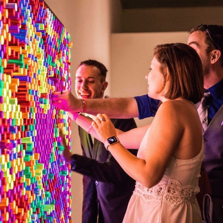 Three adults collaborating on a LiteZilla Giant Lite Brite interactive sensory light wall, creating a glowing design with colourful LitePins